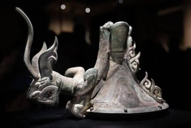 三星堆青铜鸟足神像的朱砂彩绘觚形尊上有一爬龙器盖，龙俯身在青铜立人脚下。